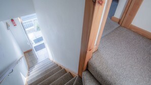 Een trap met beklede treden, houten leuningen en een deur die uitkomt in een buitenruimte.