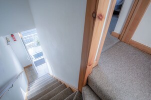 Una escalera con peldaños alfombrados, barandillas de madera y una puerta que da a un espacio exterior.