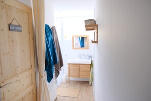 A narrow hallway leading to a bathroom with a wooden door, a towel hanging on the wall, and a small mirror above the sink. - Joli Appartement 85 m2 Avec Vues sur Montagne et Jardin Dans les Pyrénées 66 (ERR)