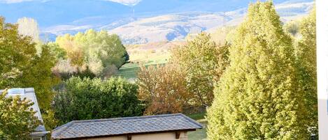 A stone building with a tiled roof, surrounded by trees and a view of distant mountains.