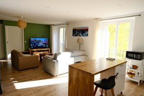 Een moderne woonkamer met een bank, een salontafel, een televisie en een eethoek met een houten tafel en stoelen.