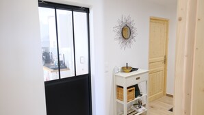 Un couloir avec un mur blanc, une porte en bois, une étagère blanche avec des paniers et un élément décoratif mural.