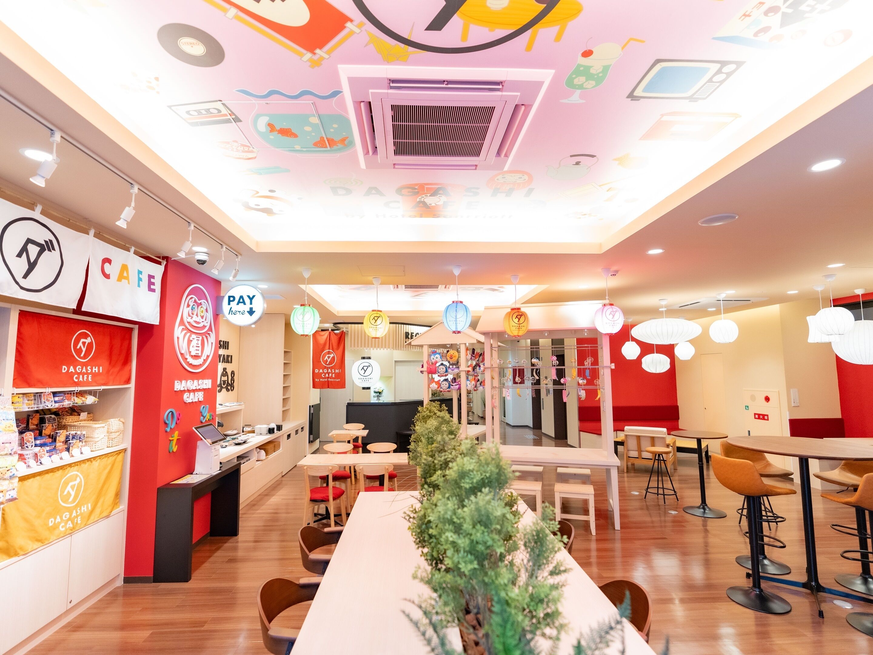 A modern cafe interior with a central seating area, a counter with a cash register, and a ceiling with colorful wall art.
