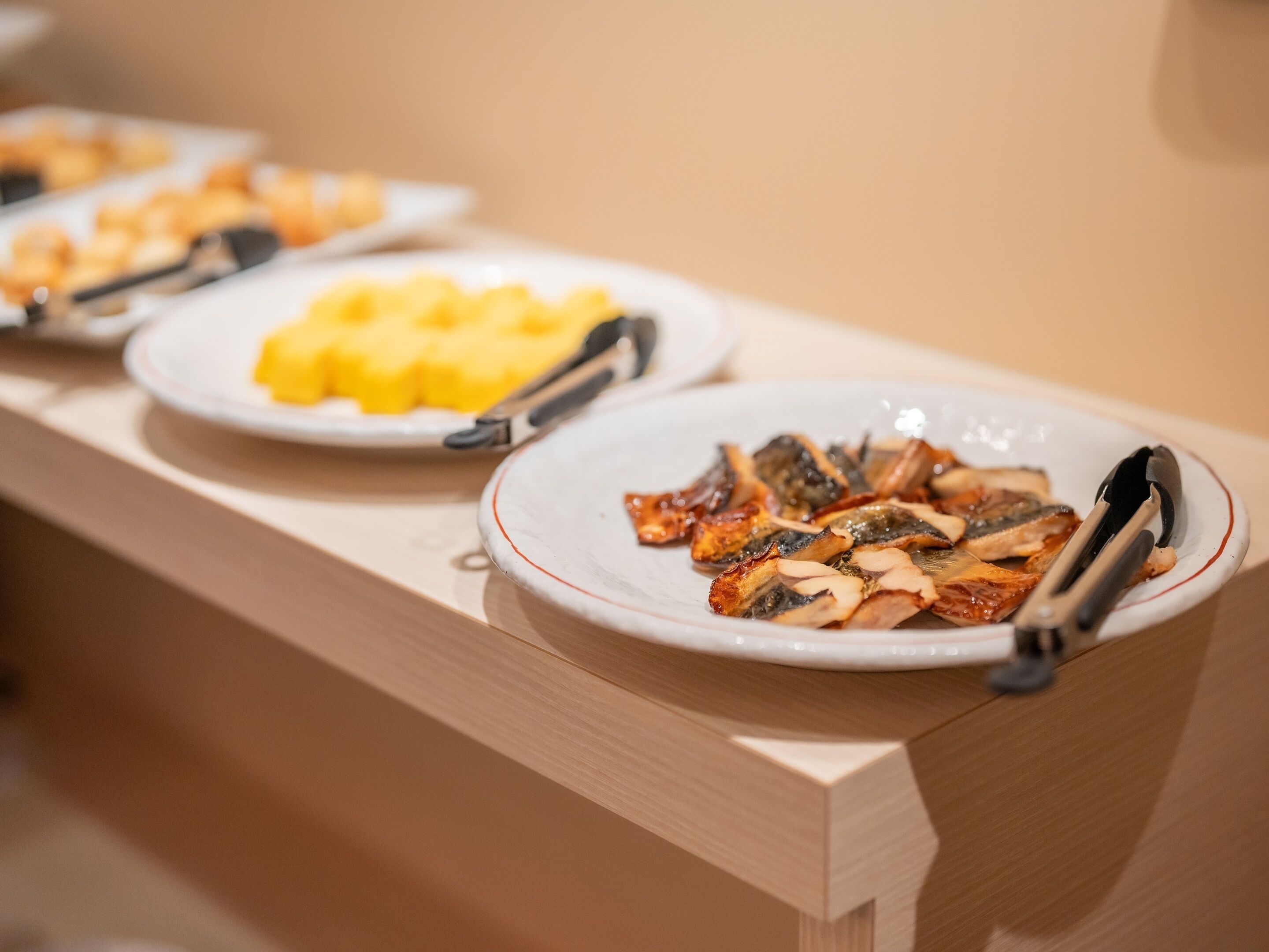 Une table de buffet garnie d’assiettes de nourriture, dont des plats qui semblent contenir du poisson grillé et des fruits jaunes.