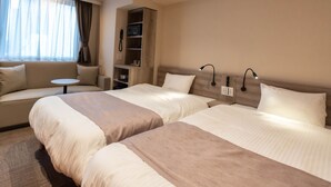 A hotel room with two beds, a sofa, a small table, and a built-in bookshelf.