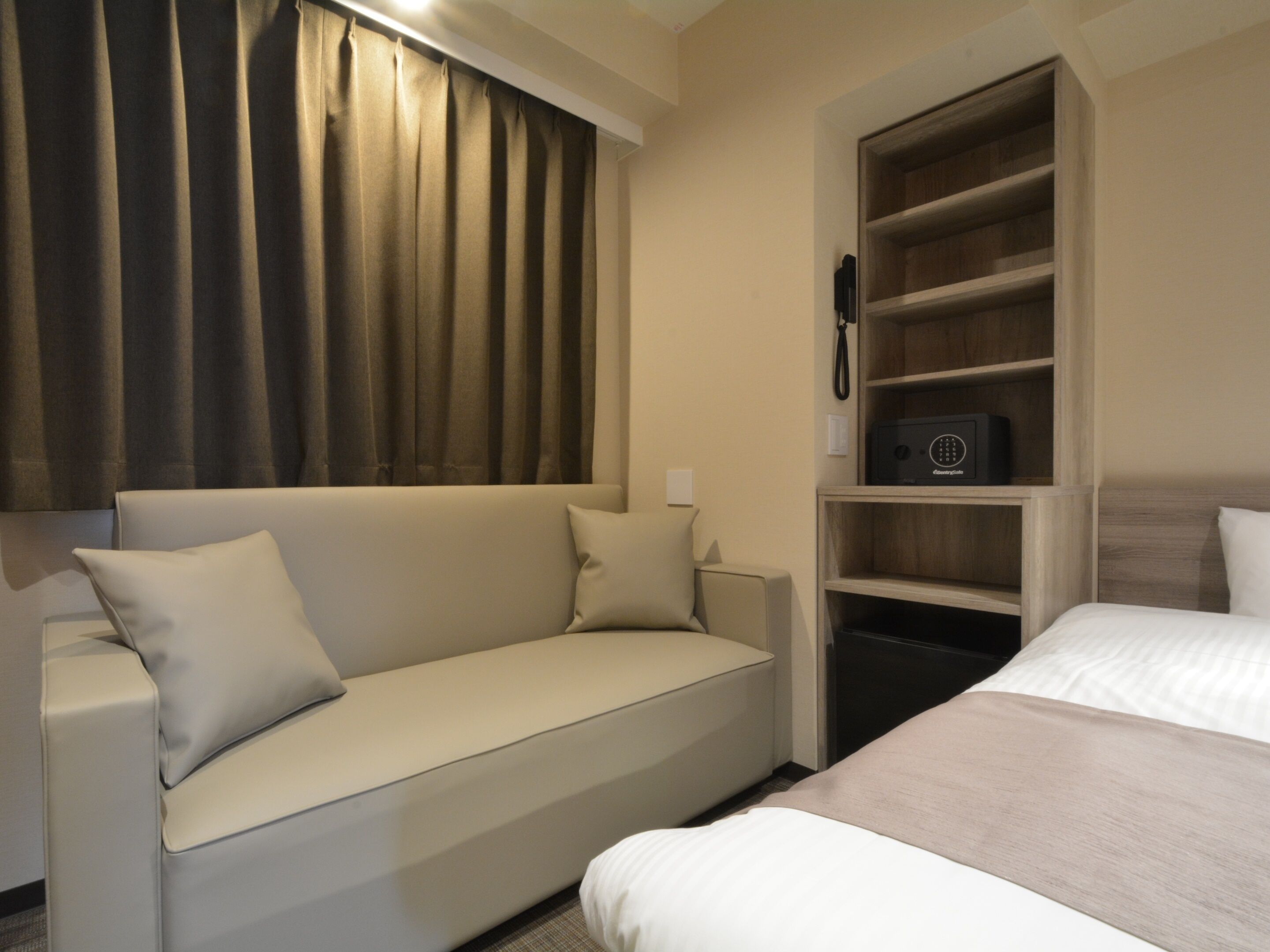Habitación de hotel con sofá, cama, estante de madera con teléfono y ventana con cortinas.