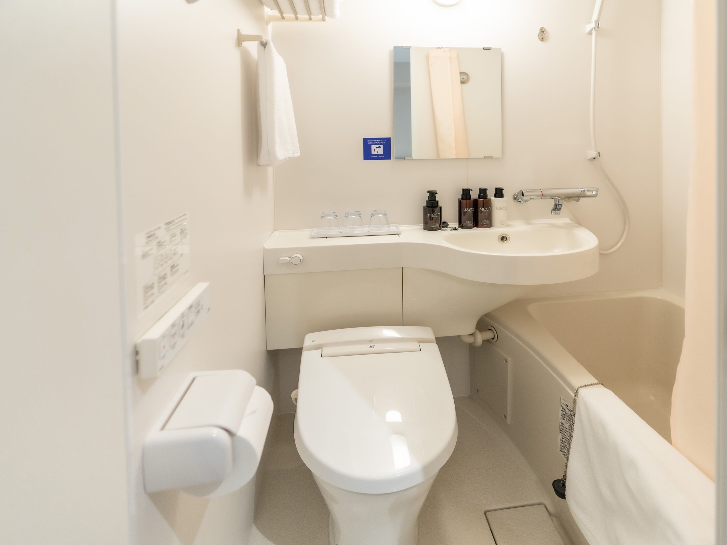 Un baño pequeño y limpio con inodoro, lavamanos y bañera. Hay artículos de aseo en la encimera.