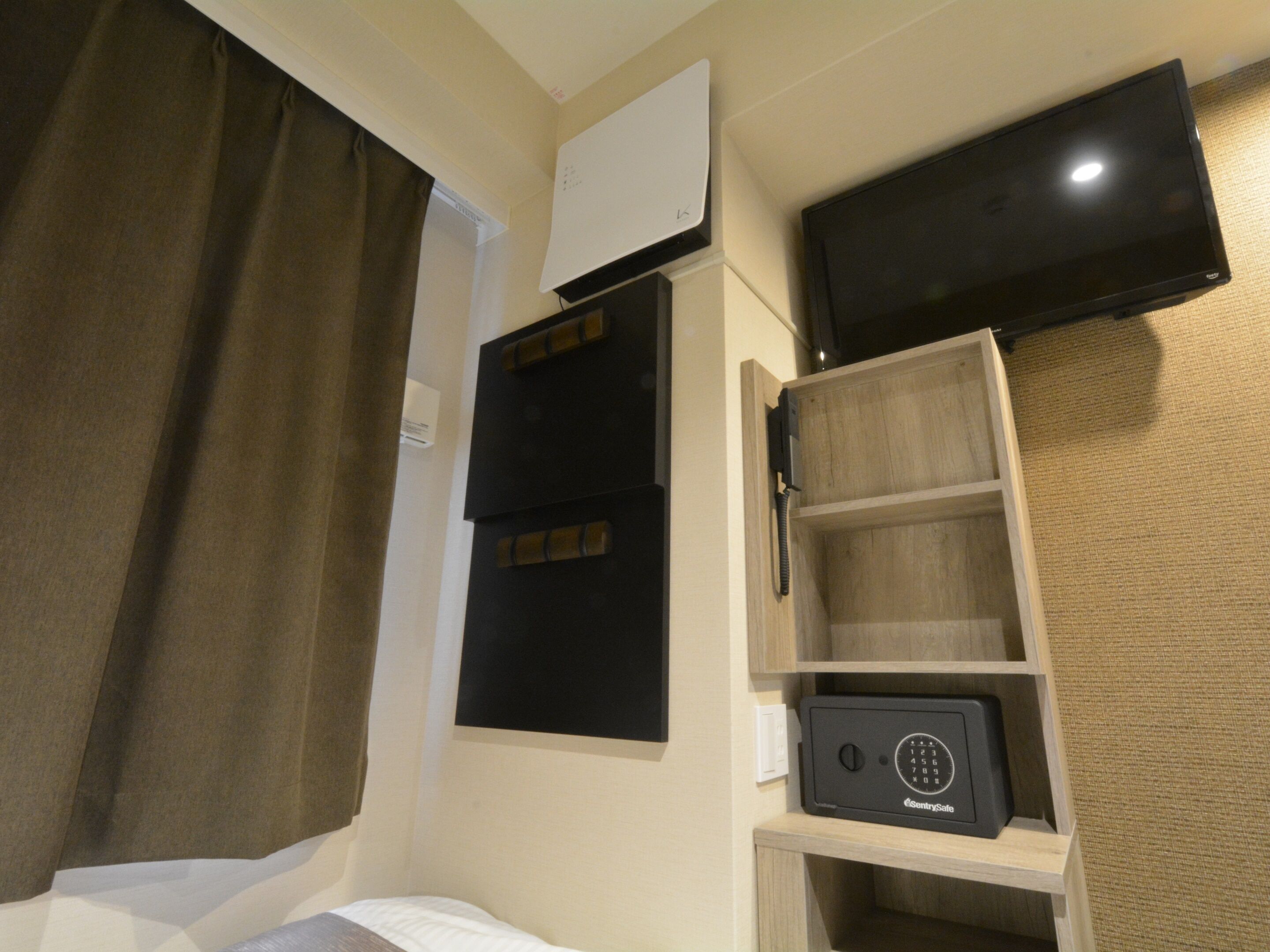 Ein Hotelzimmer mit Bett, einem an der Wand montierten Fernseher, einem Safe und einer kleinen Ablagefläche.