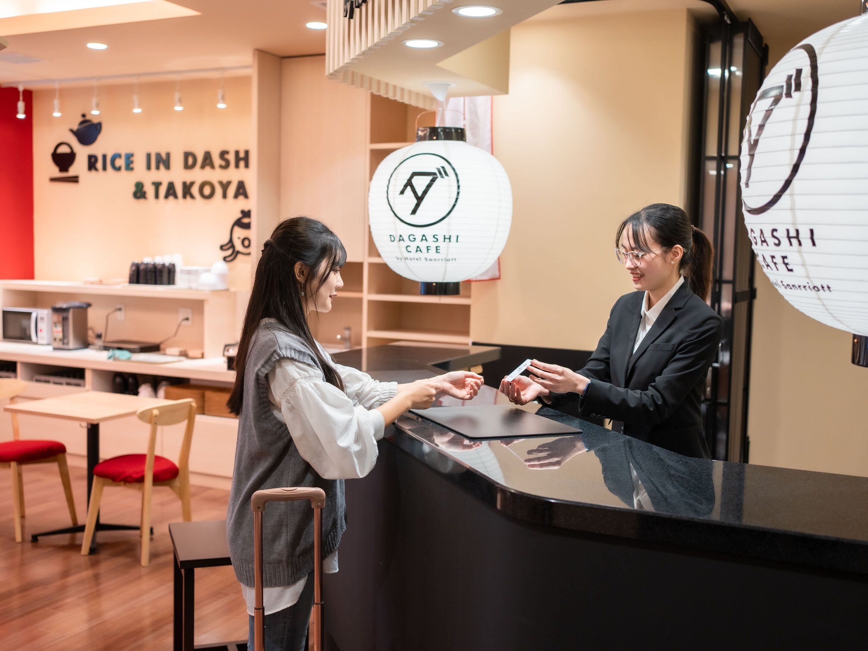 Aula, jossa on vastaanottotiski, mikroaaltouuni ja kahvinkeitin. Siellä on myös kyltit, joissa lukee ”Rice in Dash & Takoya” ja ”Dagasishi Cafe”.