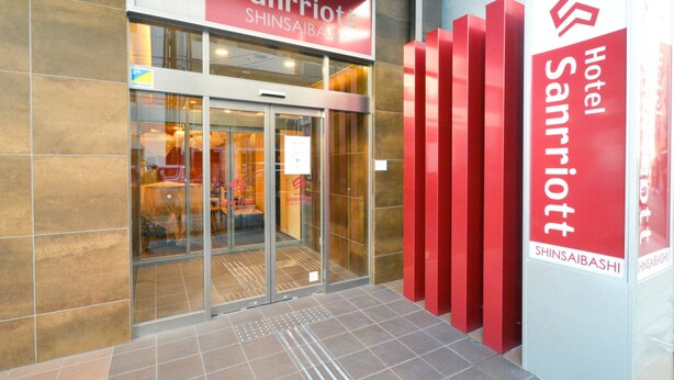 A hotel entrance with a glass door, a red sign above the door, and a red vertical sign on the right.