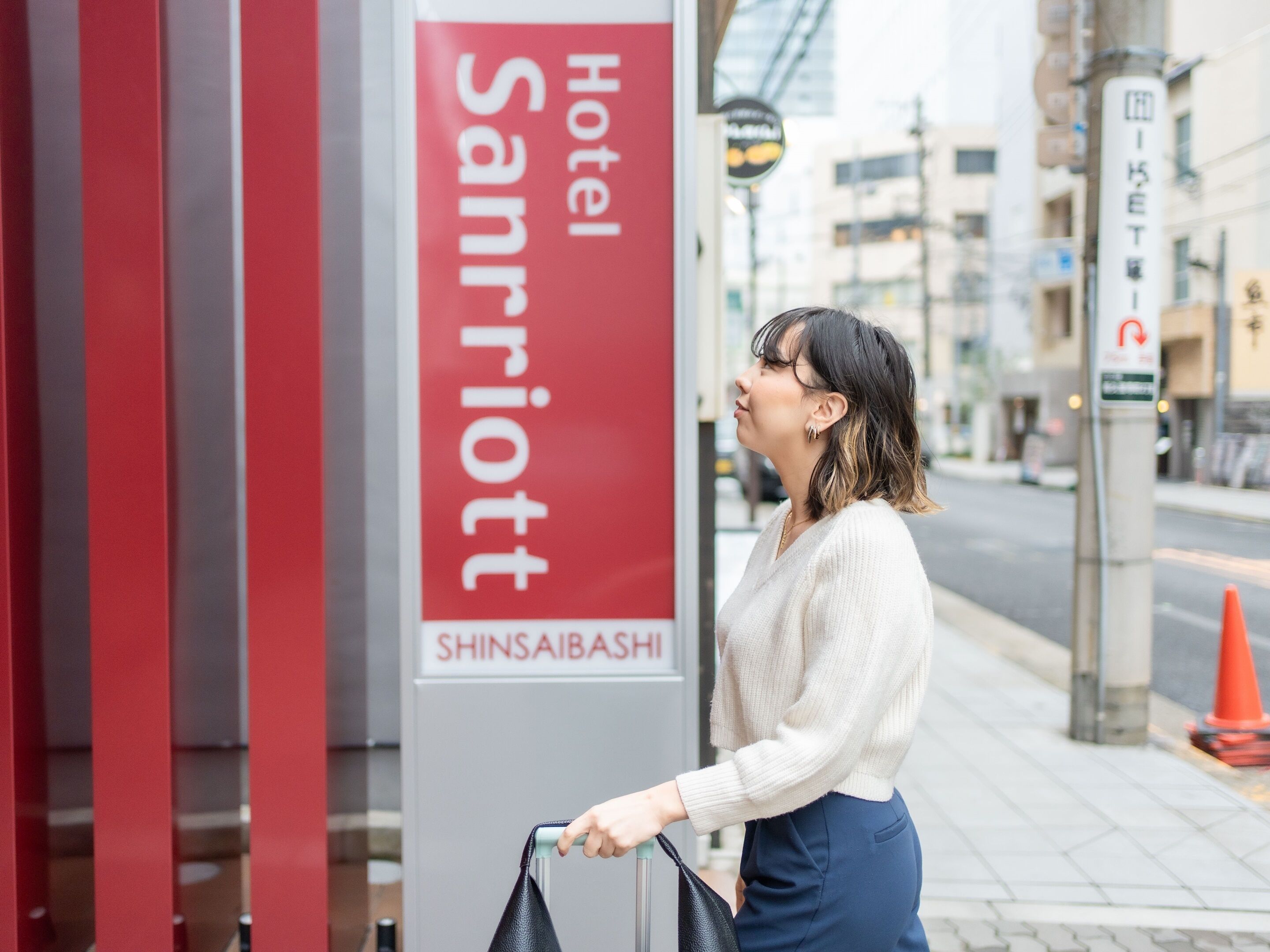 Una persona de pie frente al cartel del Hotel Sanriott Shinsaibashi.