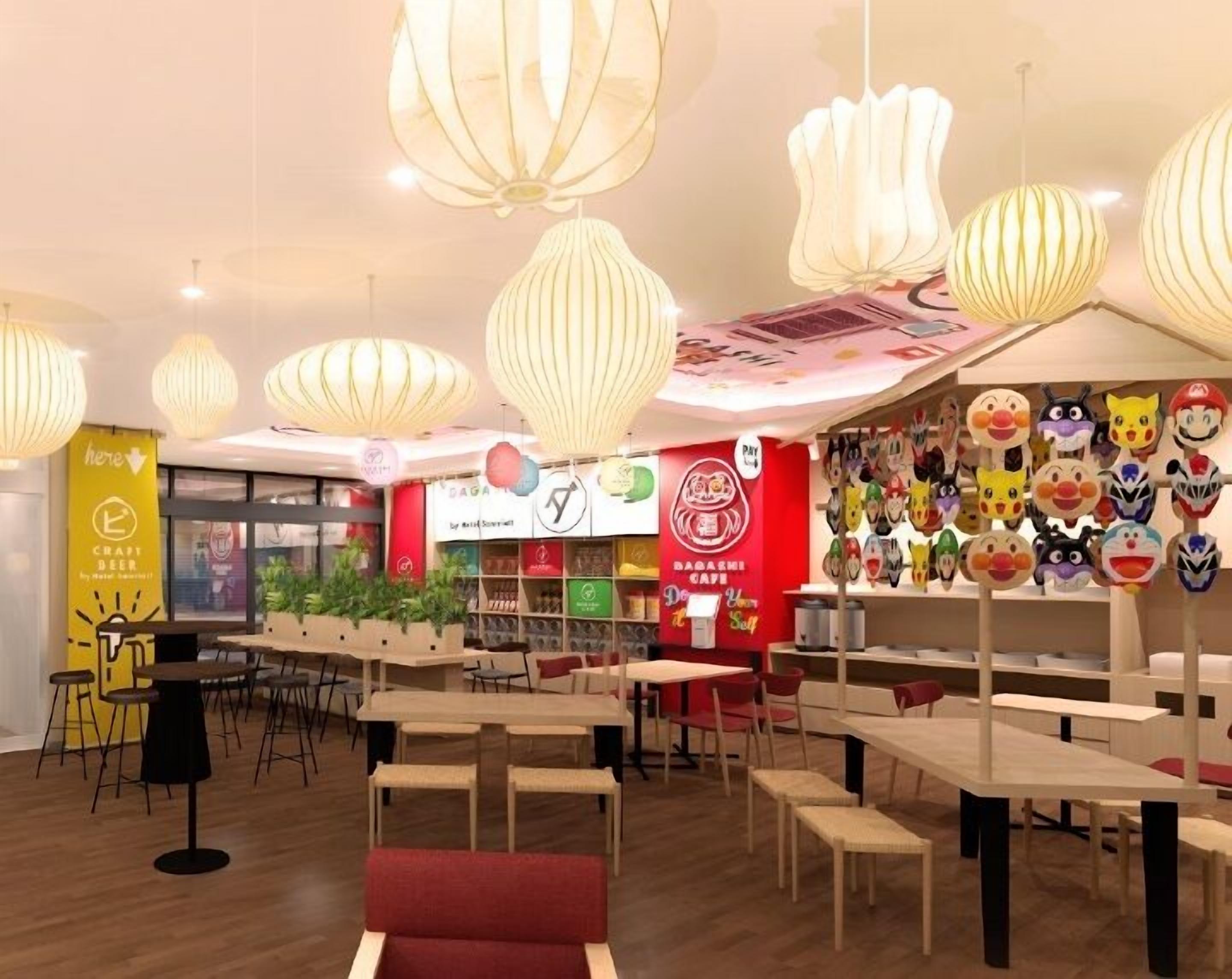 A modern cafe interior with wooden tables and chairs, hanging paper lanterns, and a wall decorated with various character masks.