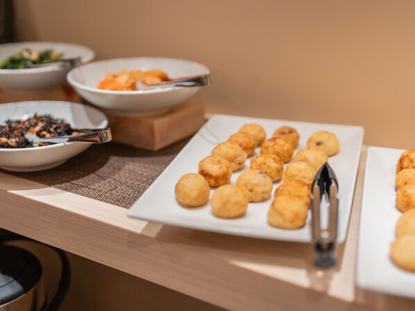 Una mesa de buffet con diversos platos, incluyendo un plato con frituras doradas, un bol de ensalada y un bol de frutos secos.
