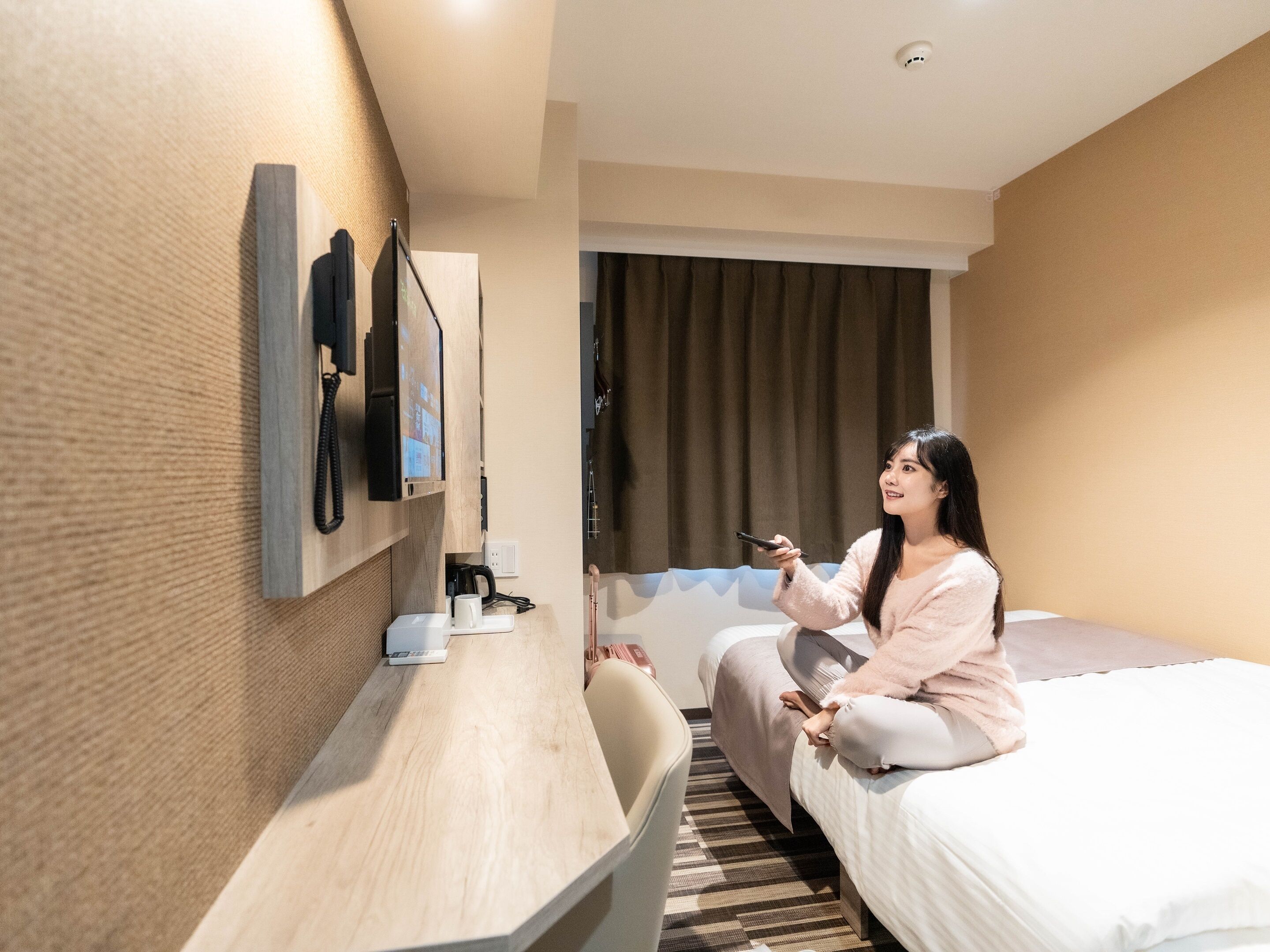 Une chambre d’hôtel équipée d’un lit, d’un bureau avec un téléphone, d’une machine à café et d’un téléviseur fixé au mur.