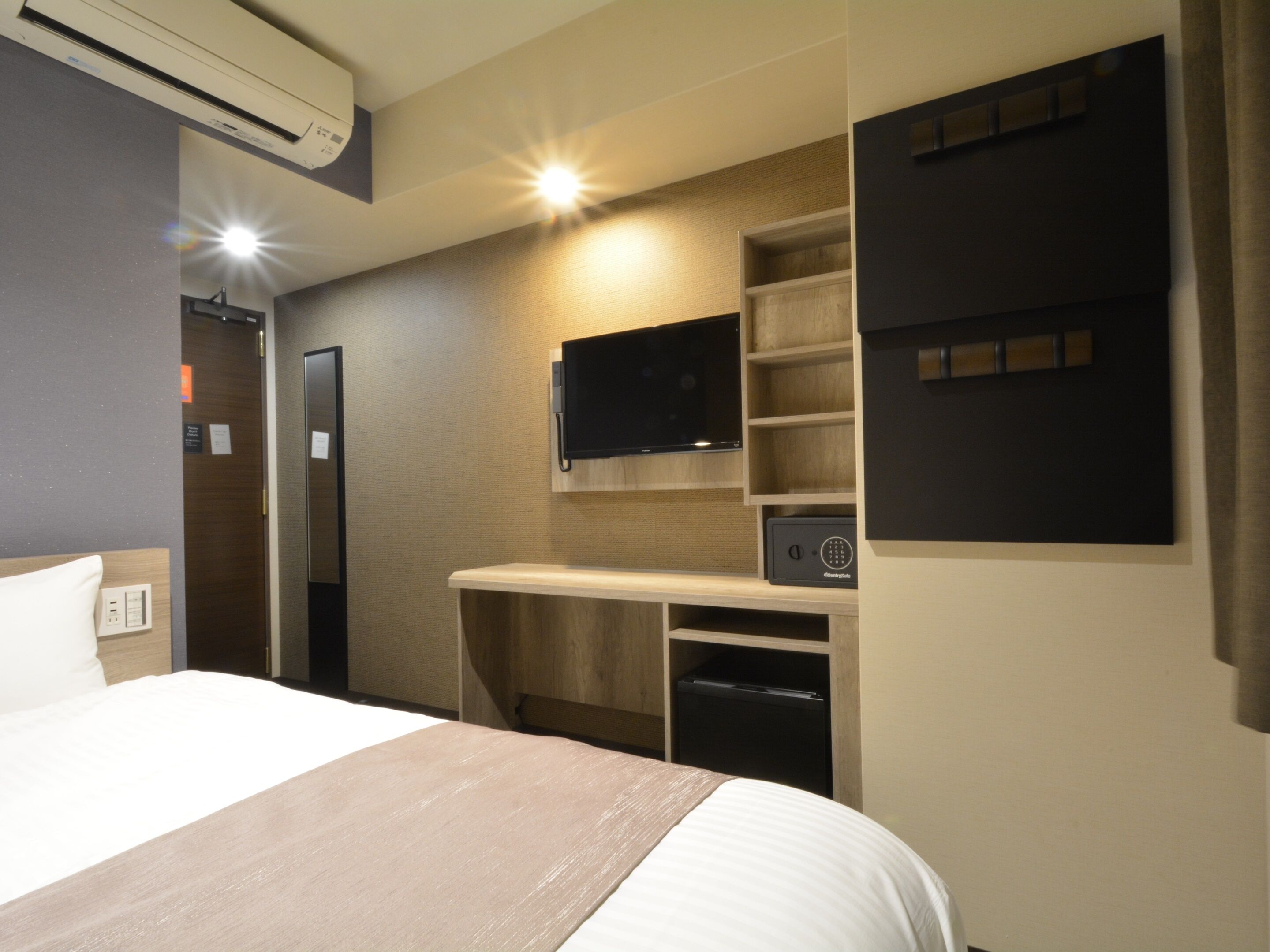 Een hotelkamer met een bed, een bureau met een flatscreen-tv, een inbouwkluis en een wandplank.