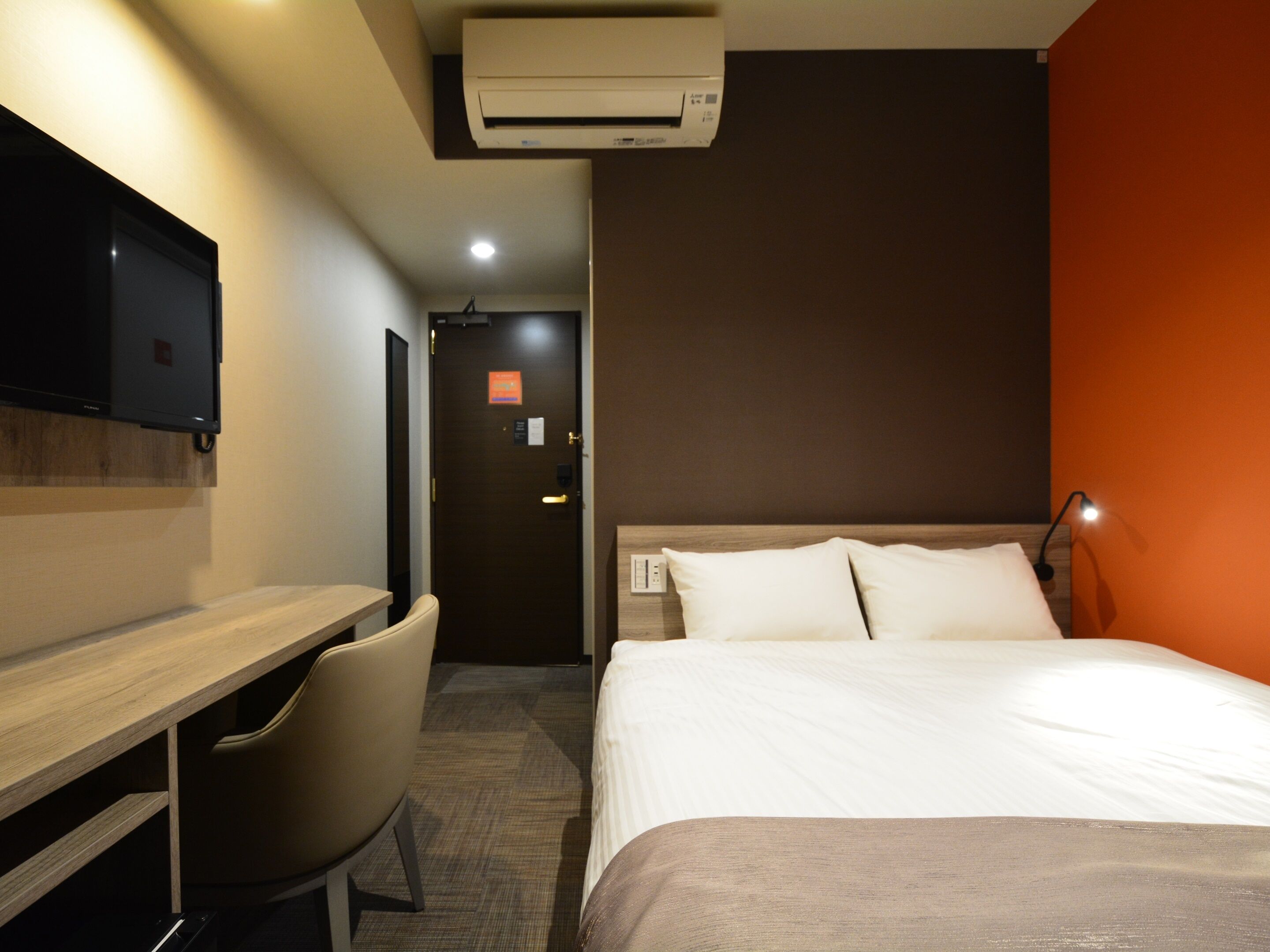 Une chambre d’hôtel équipée d’un lit, d’un bureau, d’une chaise, d’un climatiseur et d’un téléviseur.