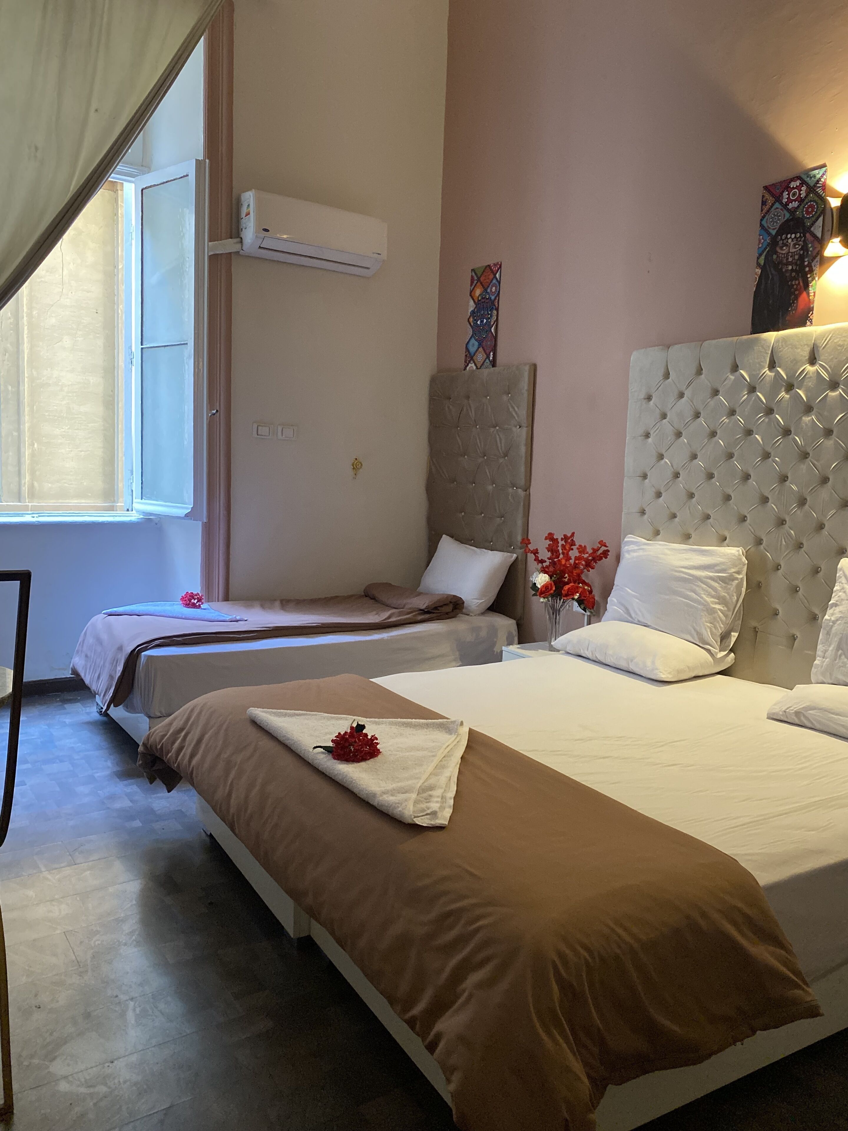 Ett hotellrum med två sängar, ett fönster med gardiner, en luftkonditioneringsanläggning och en dekorativ väggdekoration.