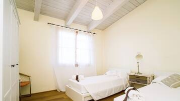 A bedroom with two beds, a wooden floor, a white wardrobe, and a bedside table with a lamp.