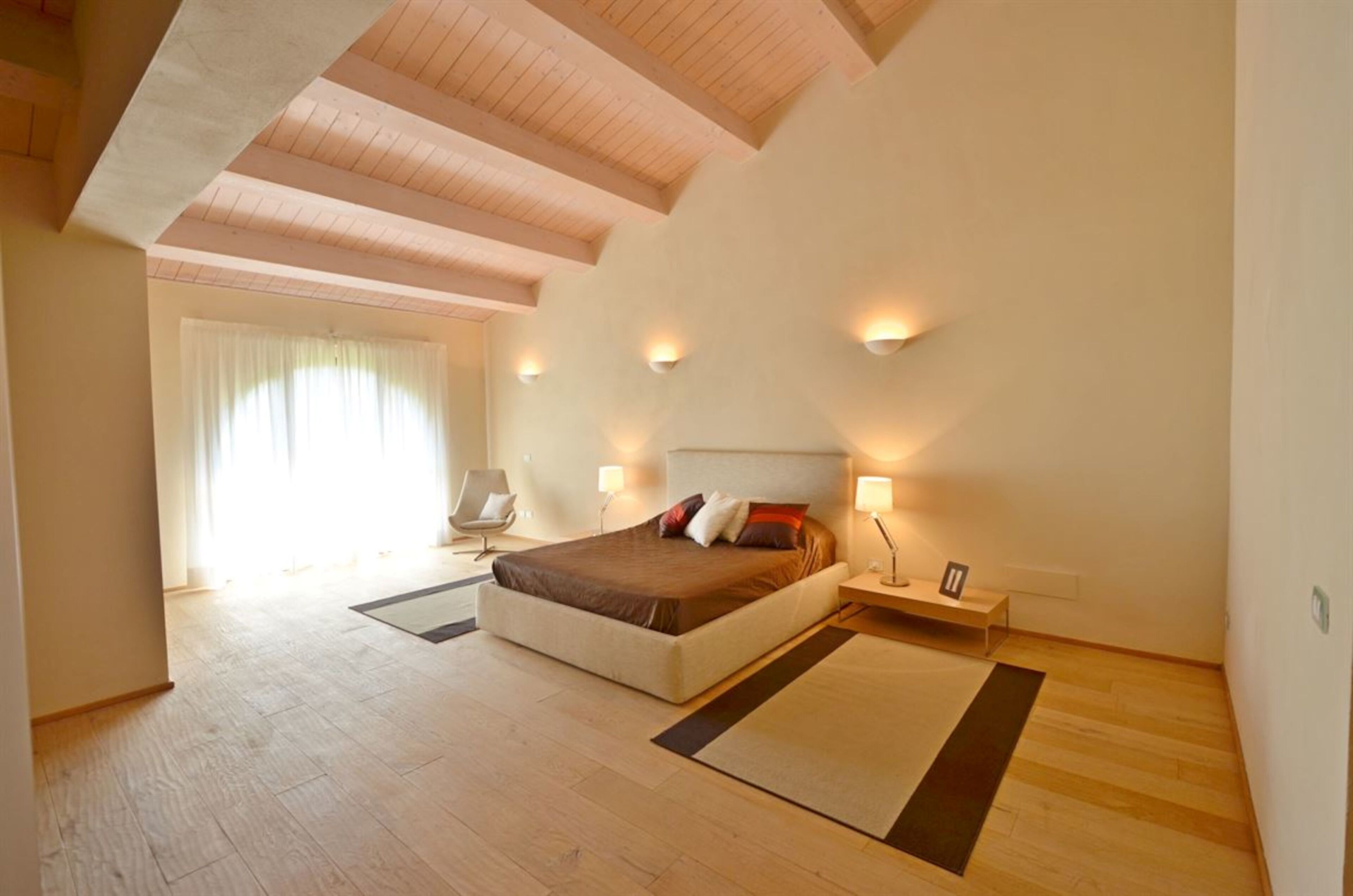 Une chambre moderne avec un grand lit, des lampes de chevet et une vue sur le paysage urbain par la fenêtre.