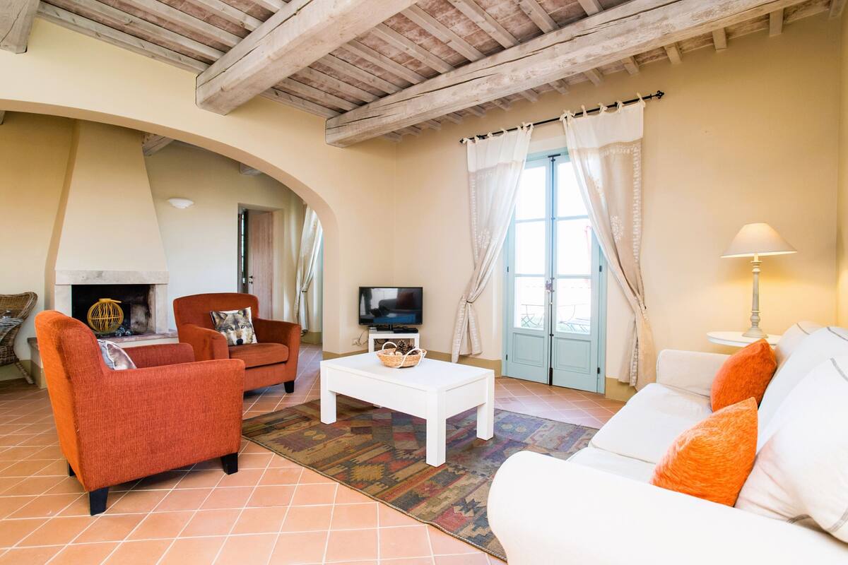 A living room with a fireplace, orange and white sofas, a white coffee table, and a television.