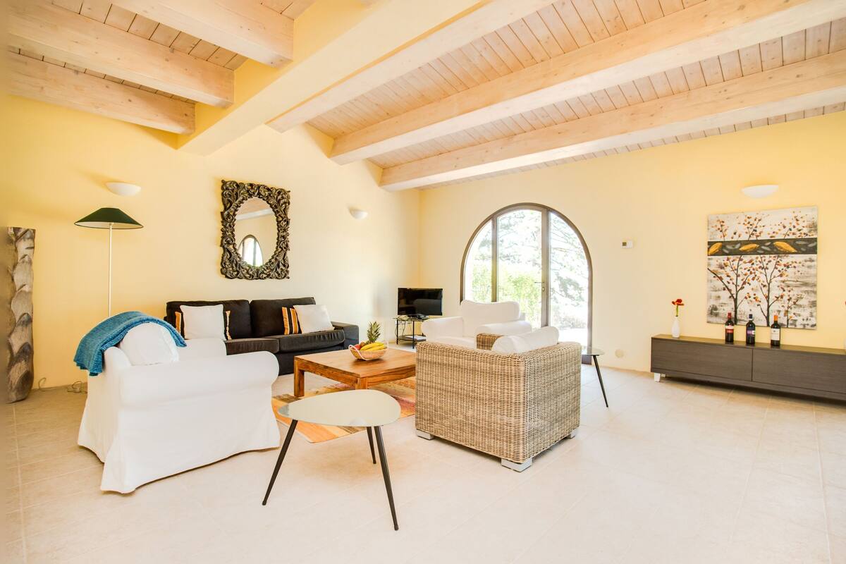 A spacious living room with a high ceiling, a large window, a fireplace, and a modern fireplace mantel.