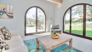 A spacious living room with a white sofa, a wooden coffee table with fruit, and large arched windows offering a view of the outdoors. - Luxury resort in the Tuscan countryside (Trequanda)