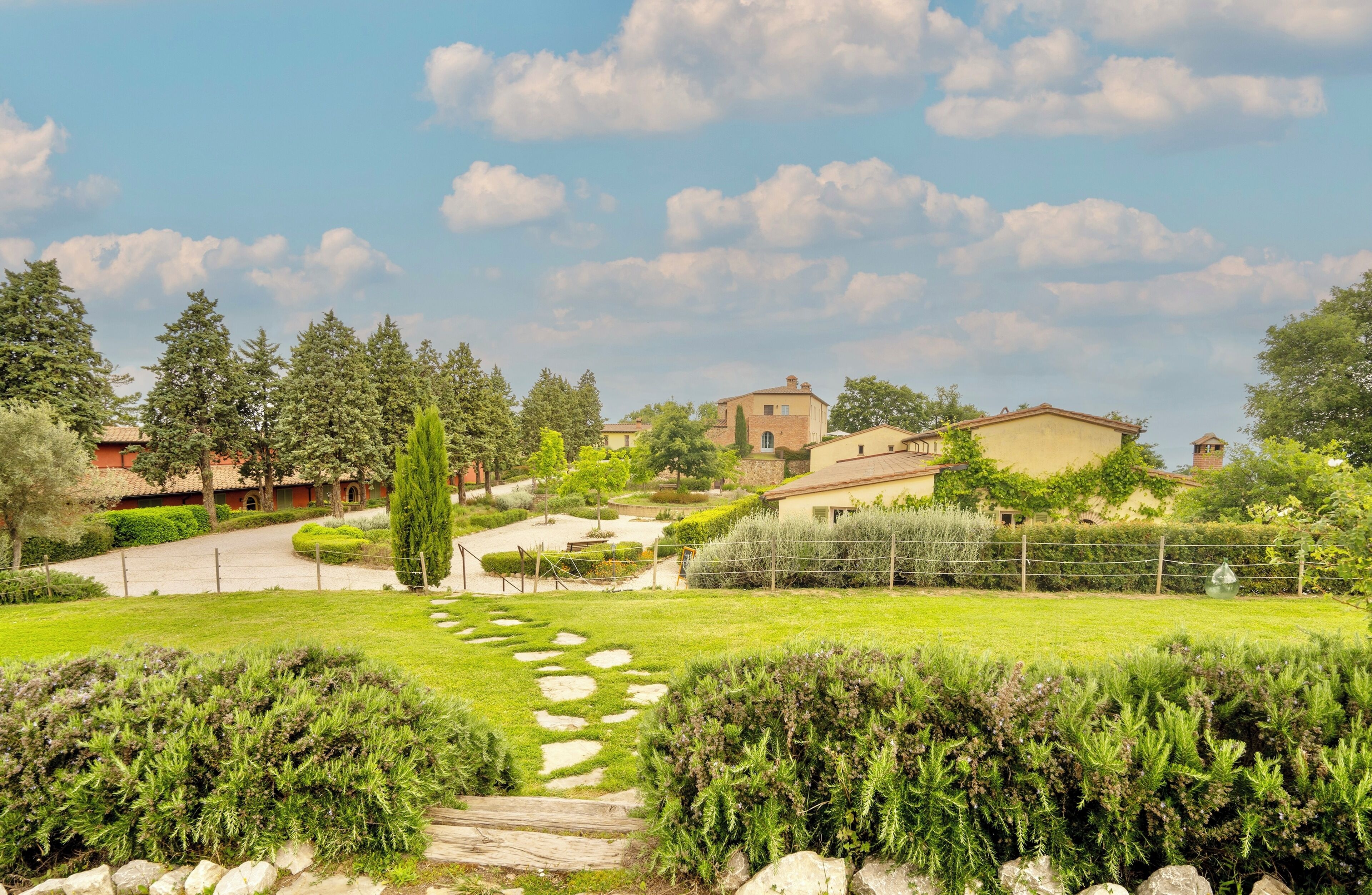 A residential area with a paved driveway leading to a house with a tiled roof, surrounded by lush greenery and trees.