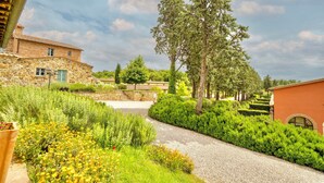 A stone building with a gravel path leading to a garden with various plants and a tree. - Luxury resort in the Tuscan countryside (Trequanda)