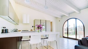A modern kitchen with a central island, white bar stools, and a large window. - Luxury resort in the Tuscan countryside (Trequanda)