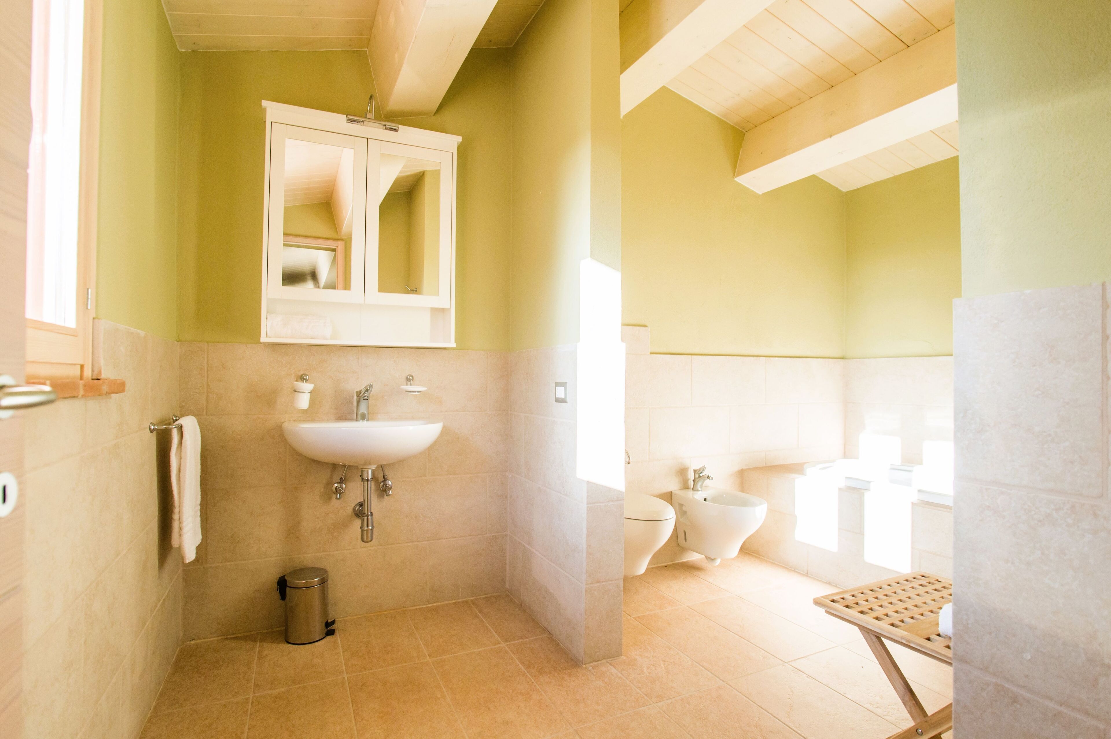 A bathroom with a sink, mirror, toilet, bidet, and a small trash can.