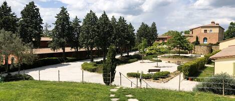 Un jardín bien cuidado con un sendero de grava, setos recortados y una variedad de árboles.