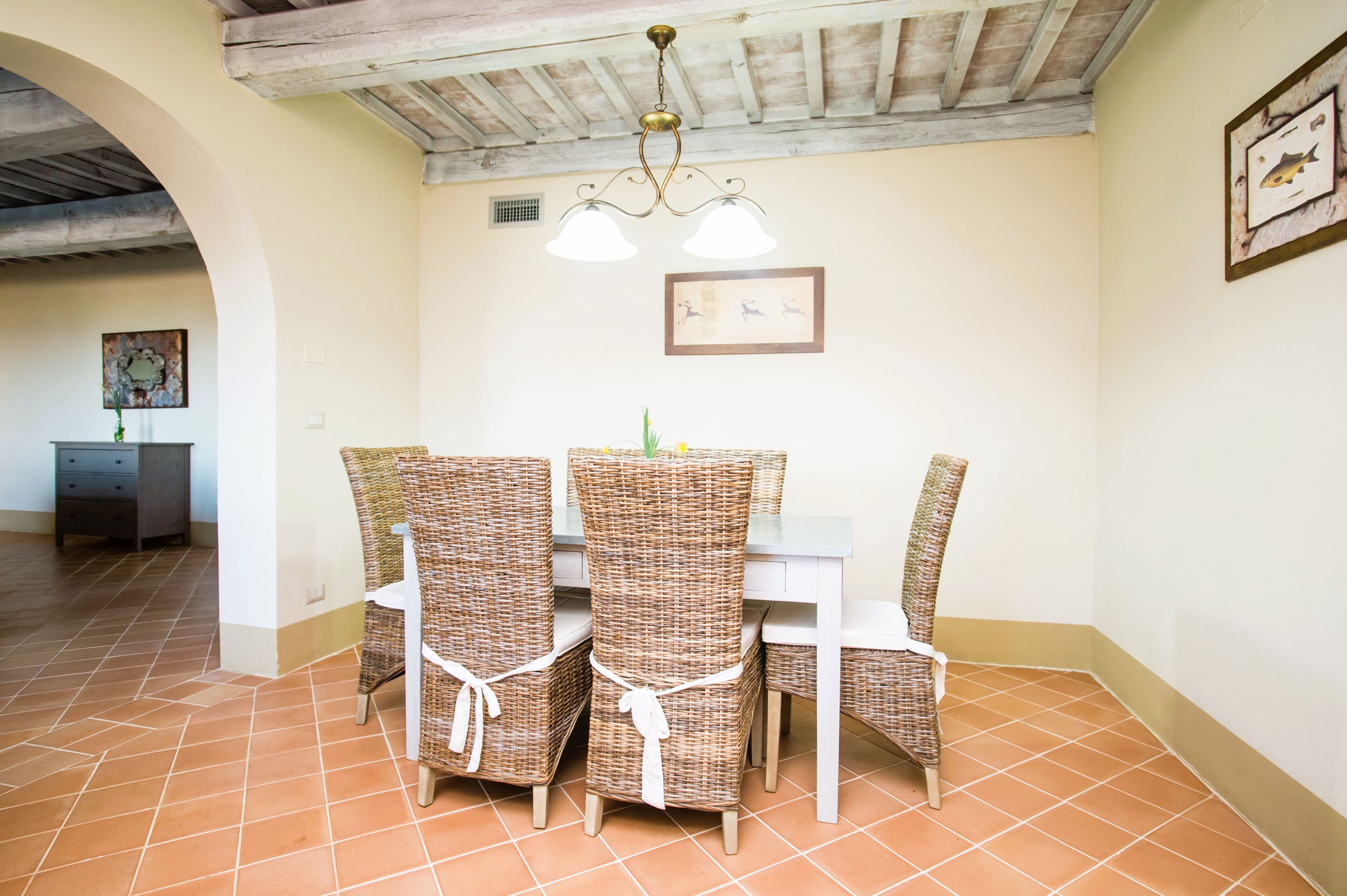 A dining area with wicker chairs and a table, a ceiling fan, and a framed picture on the wall.