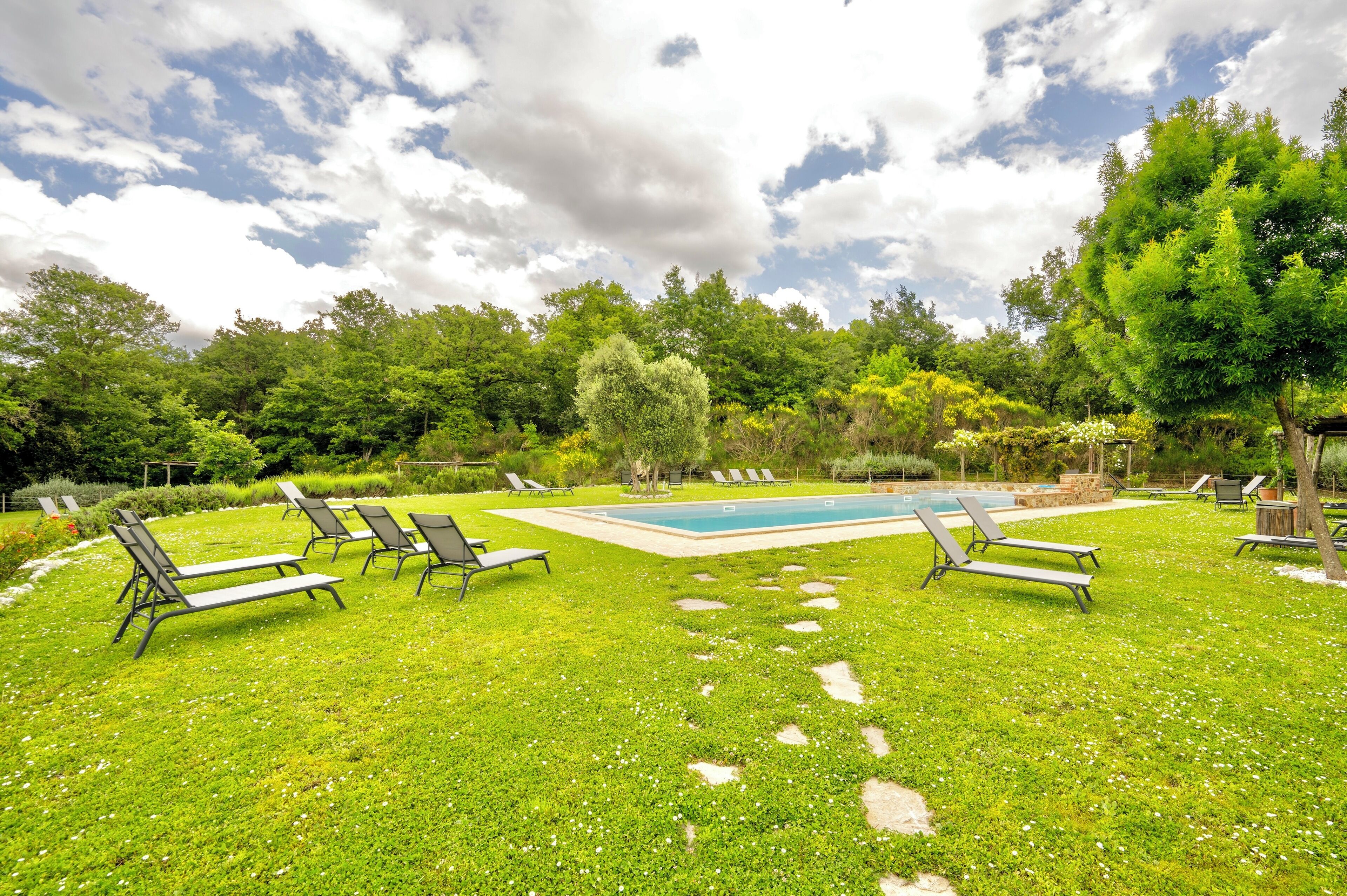 Ein Garten mit Schwimmbad, Liegestühlen und einem Kiesweg.