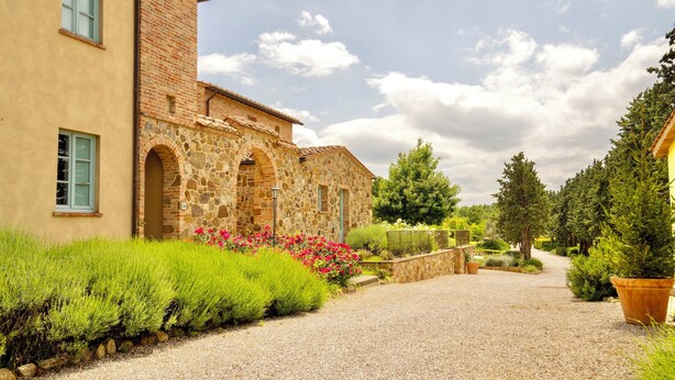 A stone building with a gravel driveway and lush greenery. - Luxury resort in the Tuscan countryside (Trequanda)