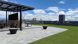 Een terras buiten met een pergola, zitplaatsen en uitzicht op de stad.