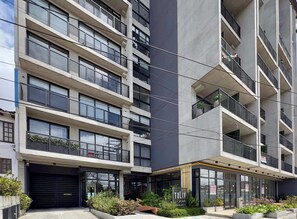 Een modern meerlaags gebouw met balkons, grote ramen en een gelijkvloerse ingang met een bord.
