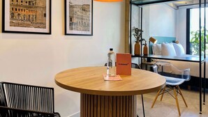 A modern room with a round wooden table, a black chair, a hanging pendant light, framed pictures on the wall, and a window with a view of greenery. - w* | Marvelous Loft in Polo (Bogotá)