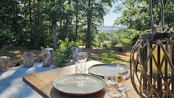 Un espace de restauration en plein air avec une table dressée pour deux personnes, entouré d’un paysage naturel et offrant une vue sur la campagne.