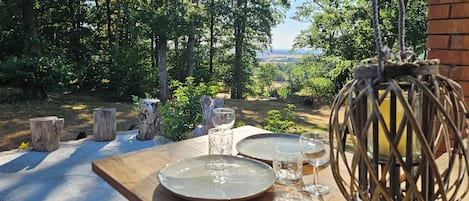 An outdoor dining area with a table set for two, surrounded by a natural landscape and a view of the countryside.