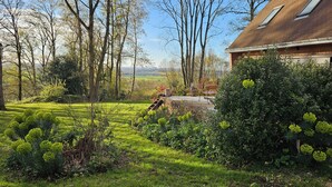 A well-maintained garden with a wooden bench, a red table, and a view of a distant landscape. - St Georges, Gîte de Campagne, 50 Minutes de Chartres, 1h du Mans 1h50 de Paris (Arcisses)