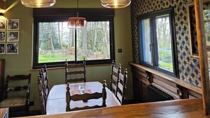A dining area with a wooden table and chairs, two hanging pendant lights, and a window with a view of trees. - St Georges, Gîte de Campagne, 50 Minutes de Chartres, 1h du Mans 1h50 de Paris (Arcisses)