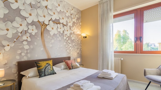 A hotel room with a bed, a wall with a floral design, a window with curtains, and a chair. - Smile House By Apulia Accommodation (Bari)