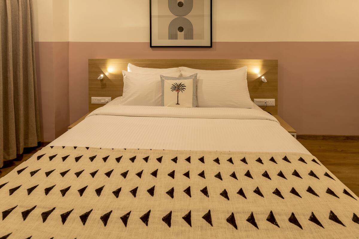 Un lit bien fait, recouvert d’une couvre-lit à motifs, agrémenté d’un seul coussin décoratif, et surmonté d’une œuvre d’art encadrée au-dessus de la tête de lit.