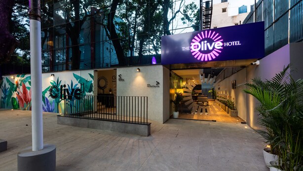 Exterior do The Olive Hotel com design moderno, um mural colorido e entrada bem iluminada.