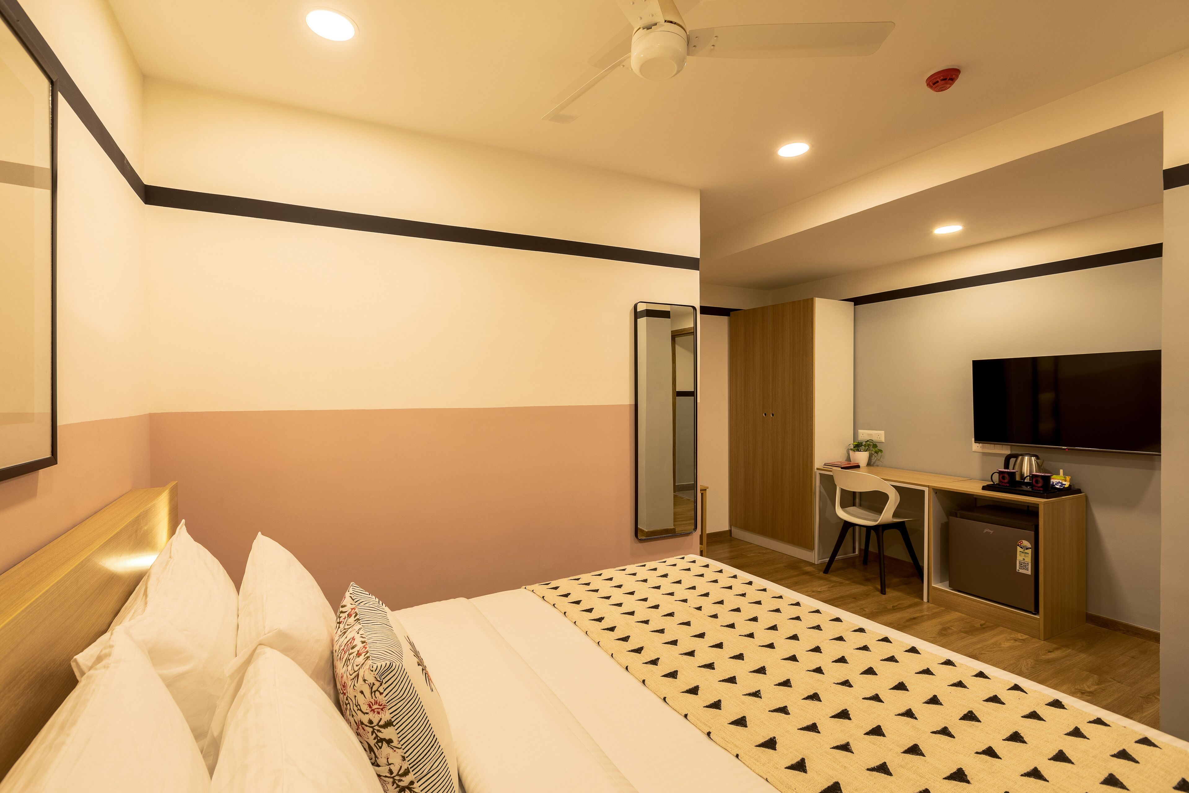 A hotel room with a bed, a desk with a chair, a TV, and a wardrobe.