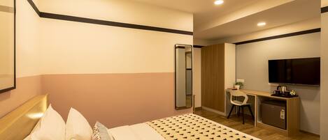 A hotel room with a bed, a desk with a chair, a TV, and a wardrobe.