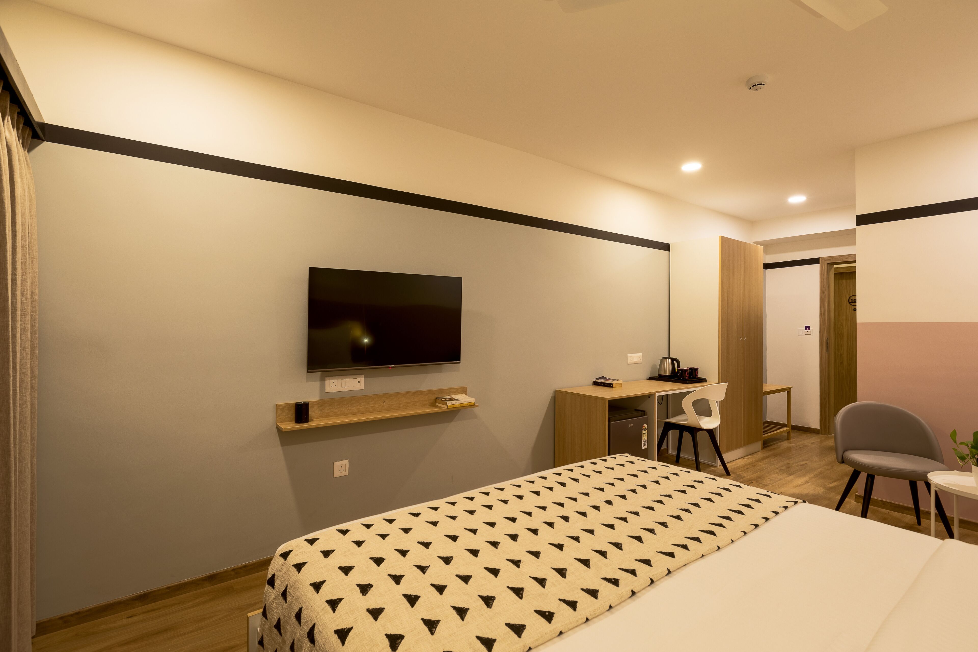 A modern hotel room with a bed, a desk, a chair, a television, and a small table.