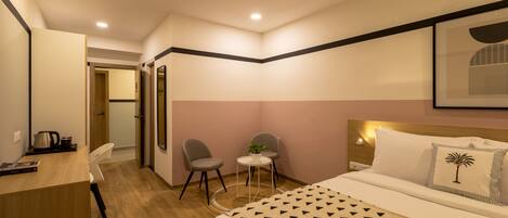 Habitación de hotel con una cama, dos sillas, una mesita con una planta y un escritorio con un hervidor.
