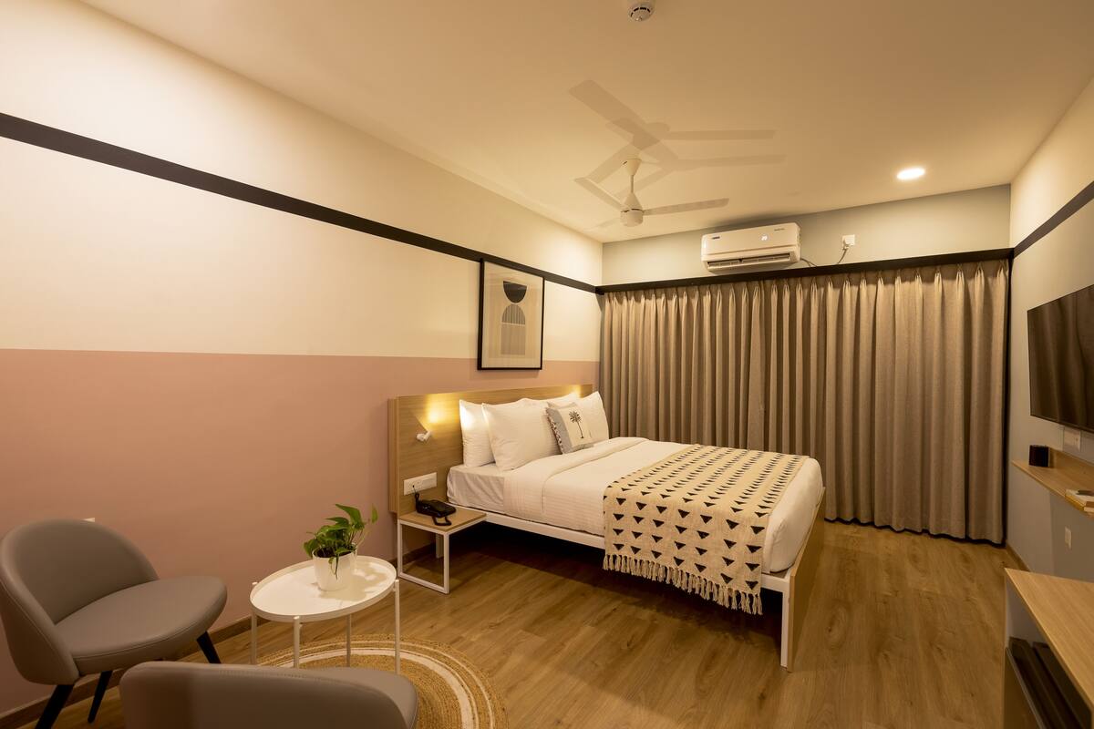 Une chambre d’hôtel moderne équipée d’un lit, d’une table de chevet, d’une chaise et d’une petite table agrémentée d’une plante.