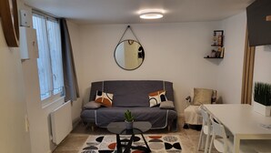 A compact living space with a sofa, a dining table, a small rug, and a mirror on the wall. - Duplex Hyper Centre-ville (Quimper)